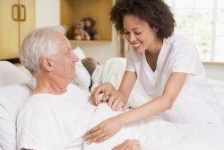 A nurse is talking to an elderly man in a hospital bed.