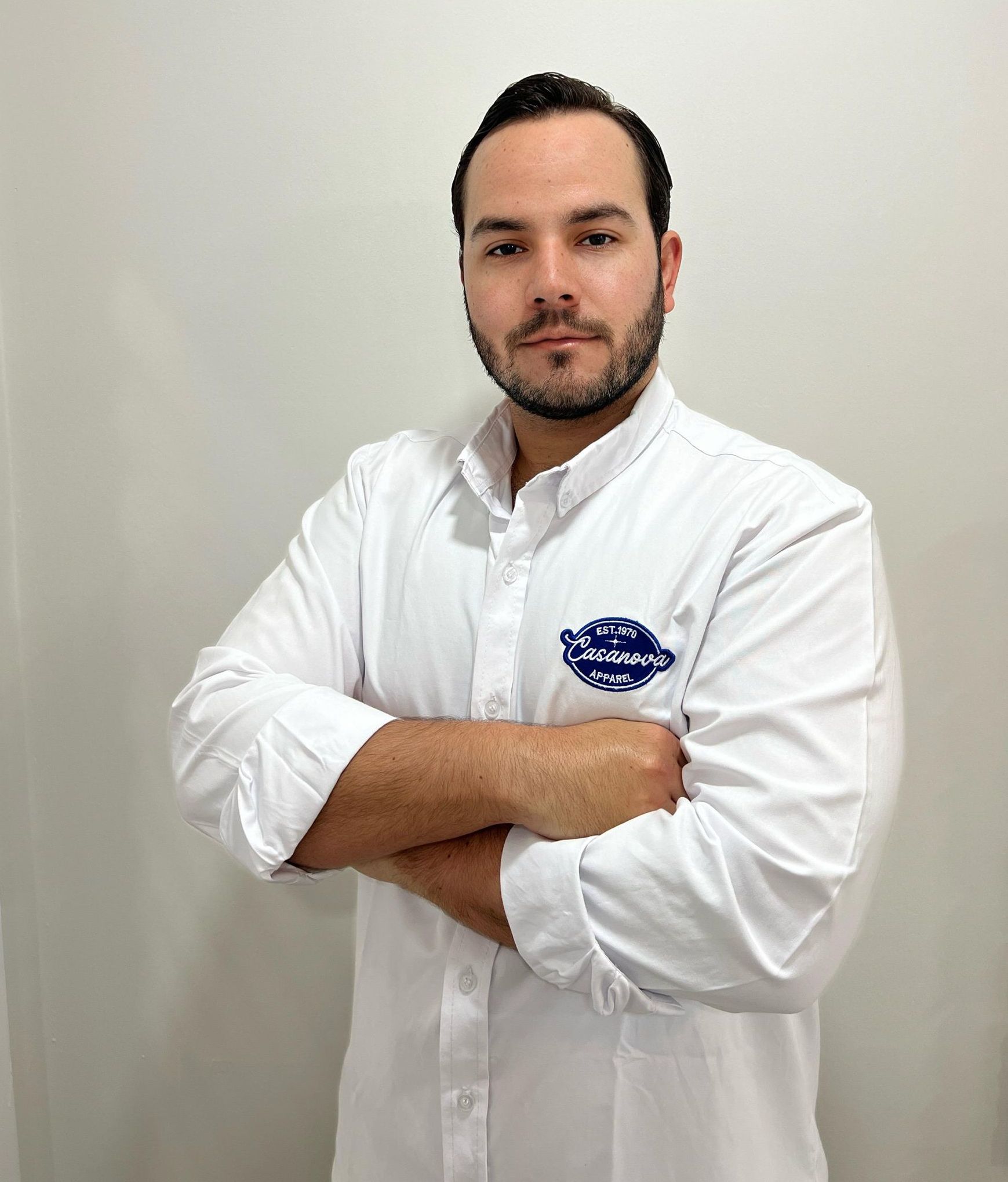 Un hombre con barba que lleva una camisa blanca y los brazos cruzados.