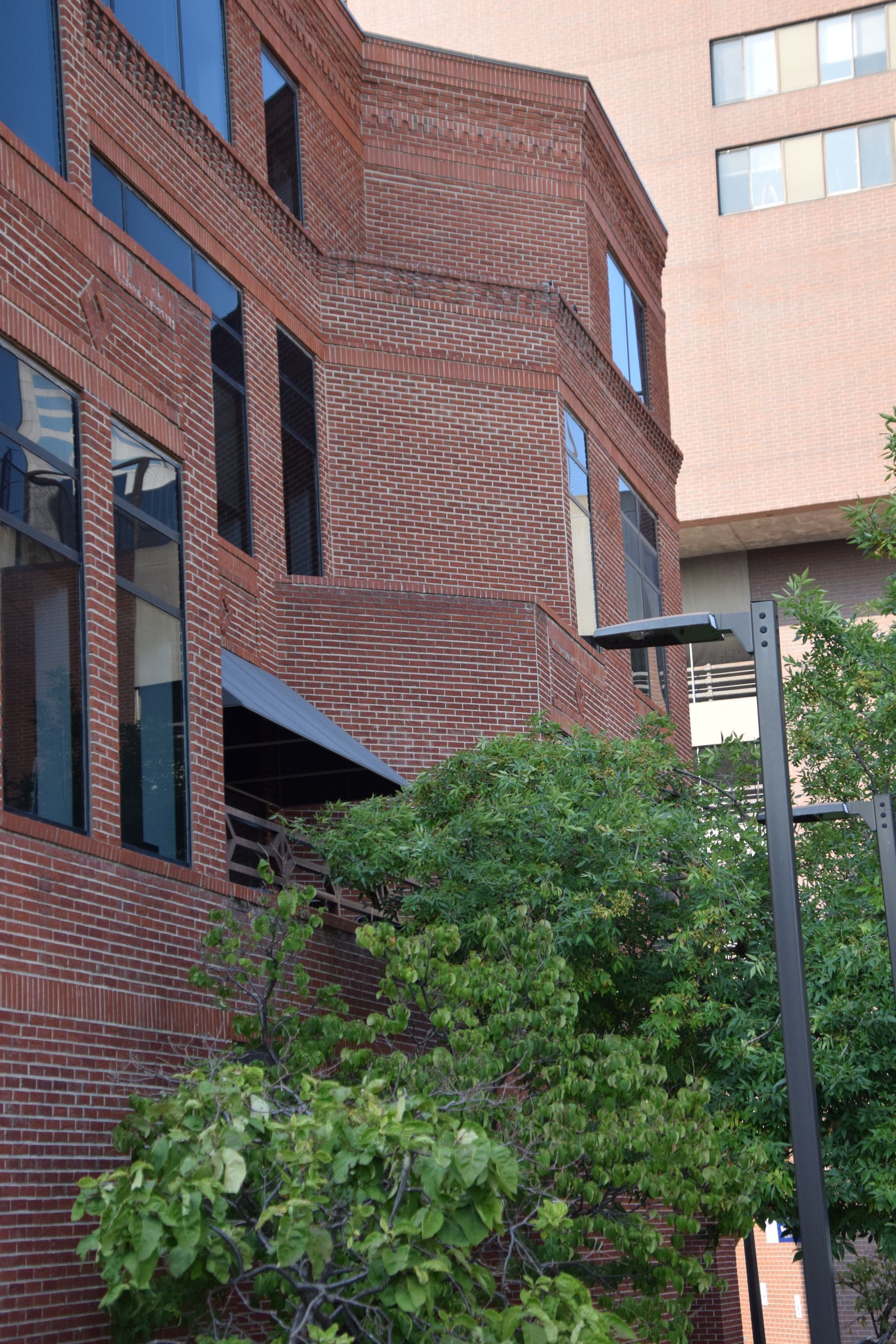 Brick building with large windows and a small awning, partially obscured by green foliage.