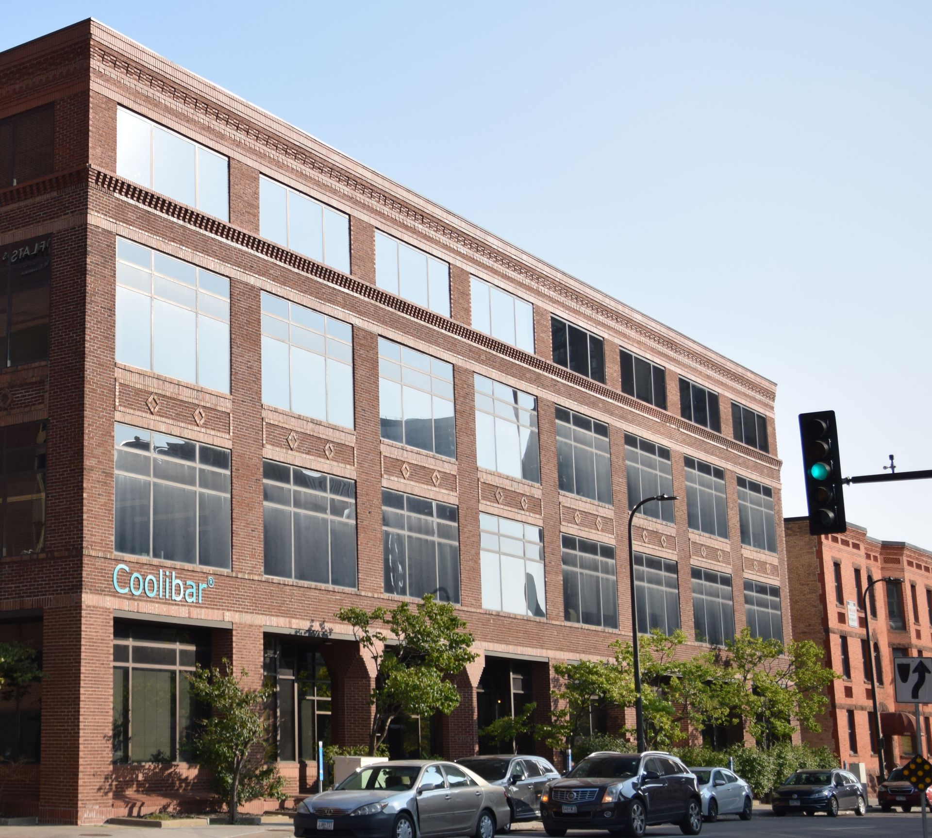 Brick building with large windows, cars on street. 