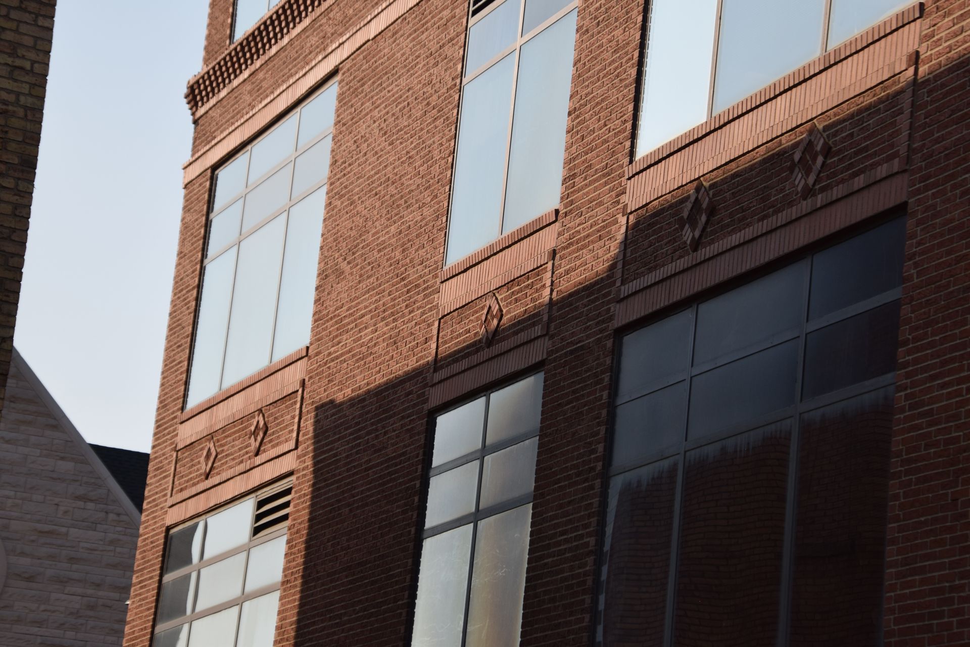 Brick building with large windows reflecting the sky; a shadow falls across a portion of the facade.