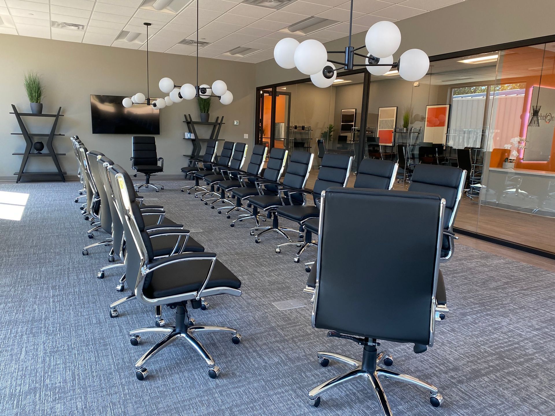 A conference room with rows of black chairs, a large TV monitor, and modern light fixtures.