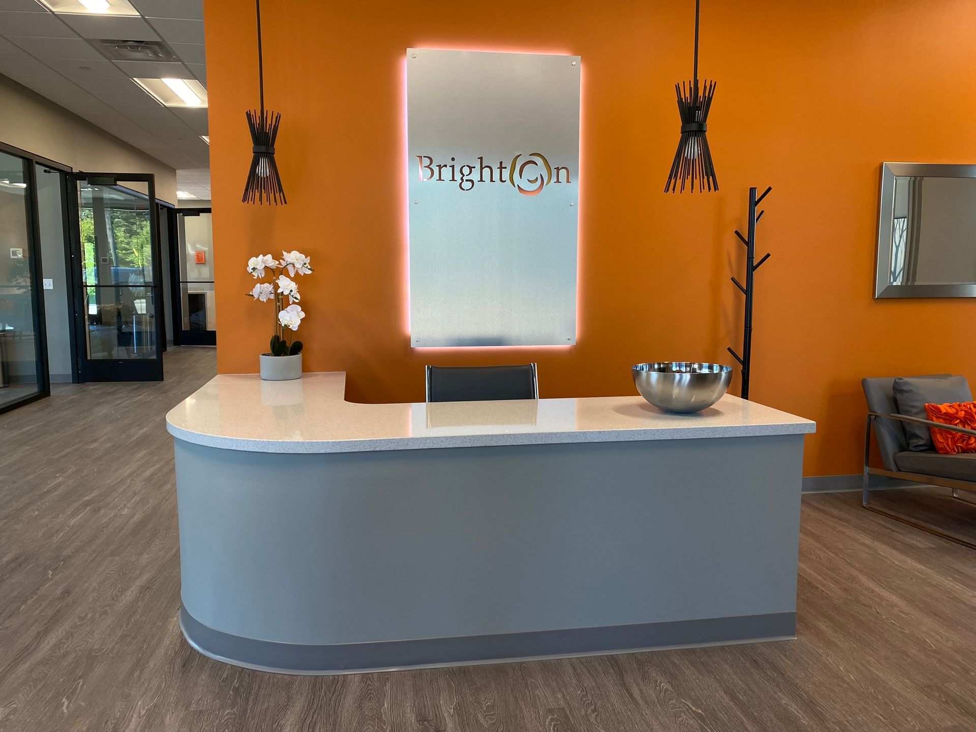 Reception desk with Brighton logo, orange wall, gray desk, and flower arrangement.