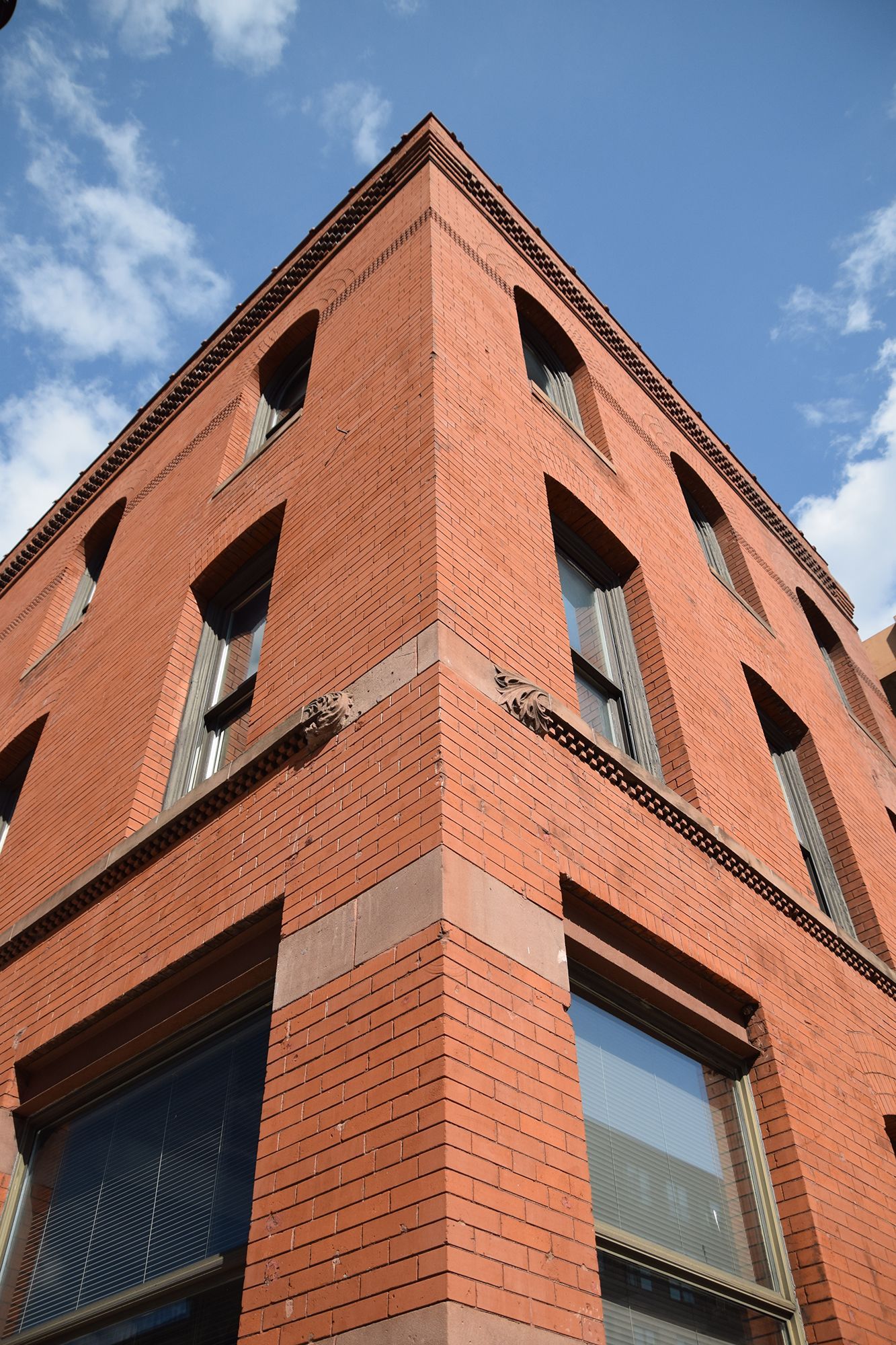 Red brick building corner with windows against a blue sky.