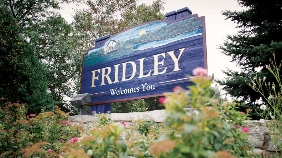 Fridley city welcome sign with blue background, trees, and flower bushes.