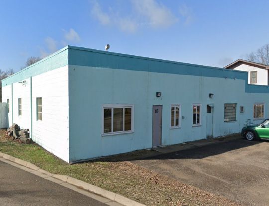 Light blue one-story building with teal trim, windows, and a green car parked outside.