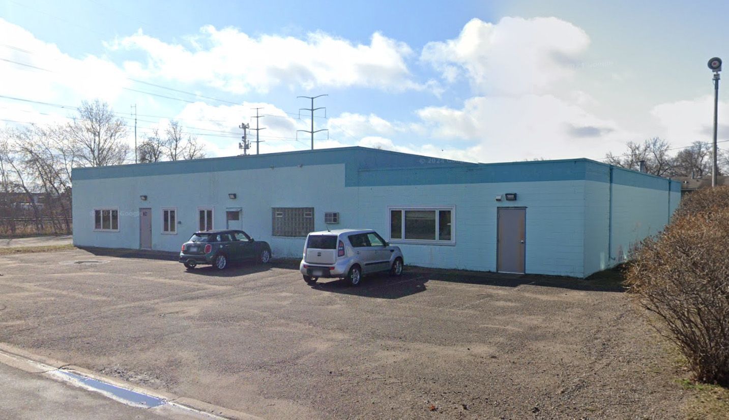 Light blue building with two cars parked out front on a partly cloudy day.