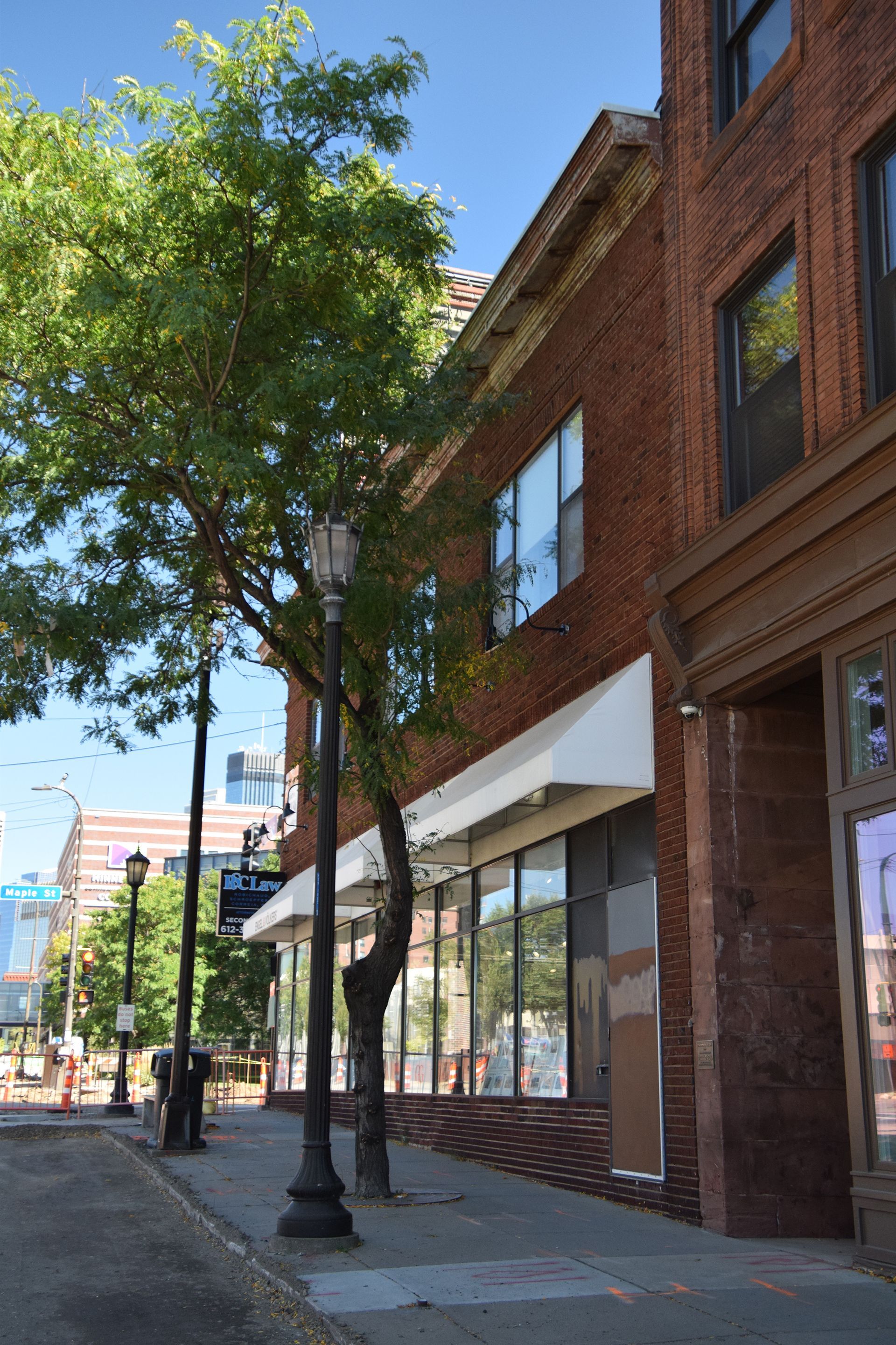 Brick building with storefronts, street, and tree. Blue sky.