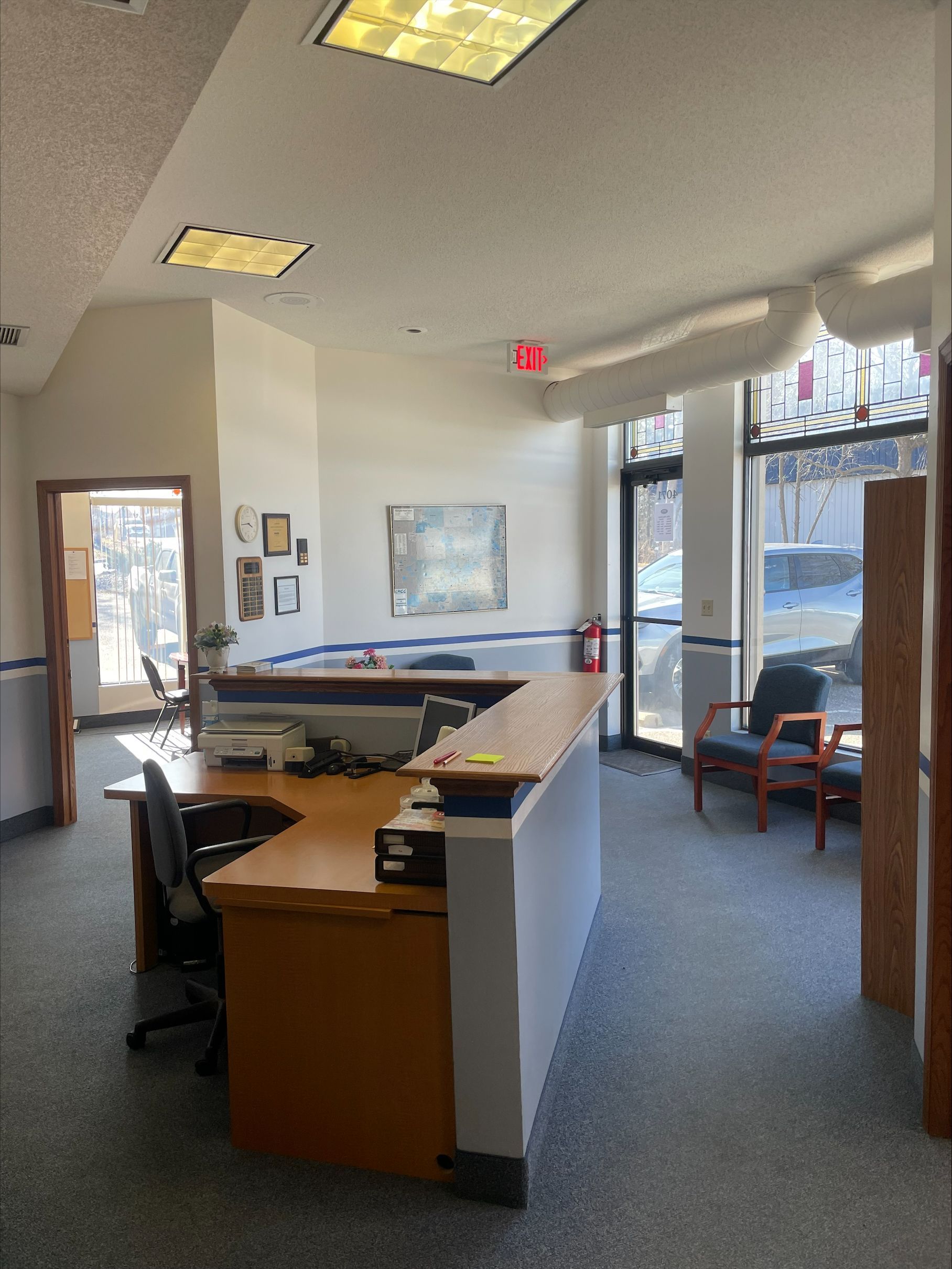 Office reception area with a curved desk, chairs, and an exit door.