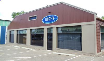 Brown building with large windows, a building sign, and a parking lot.
