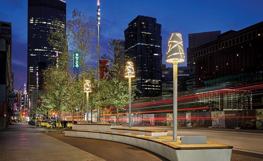 Street scene at night with benches, decorative streetlights, and city buildings in the background.