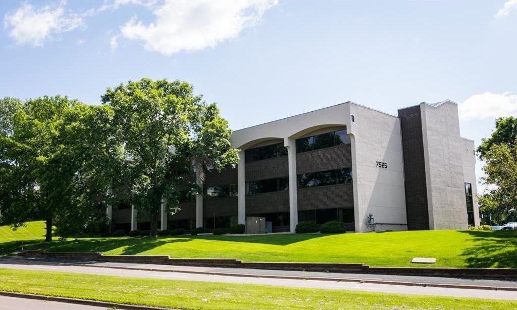 Office building with a white facade, dark brown accents, and green lawn under a blue sky.