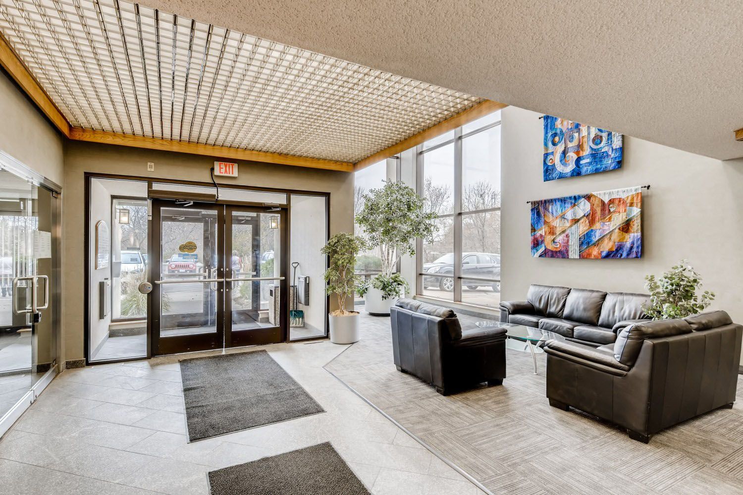 Lobby with double glass doors, black leather couches, art, and a large window.