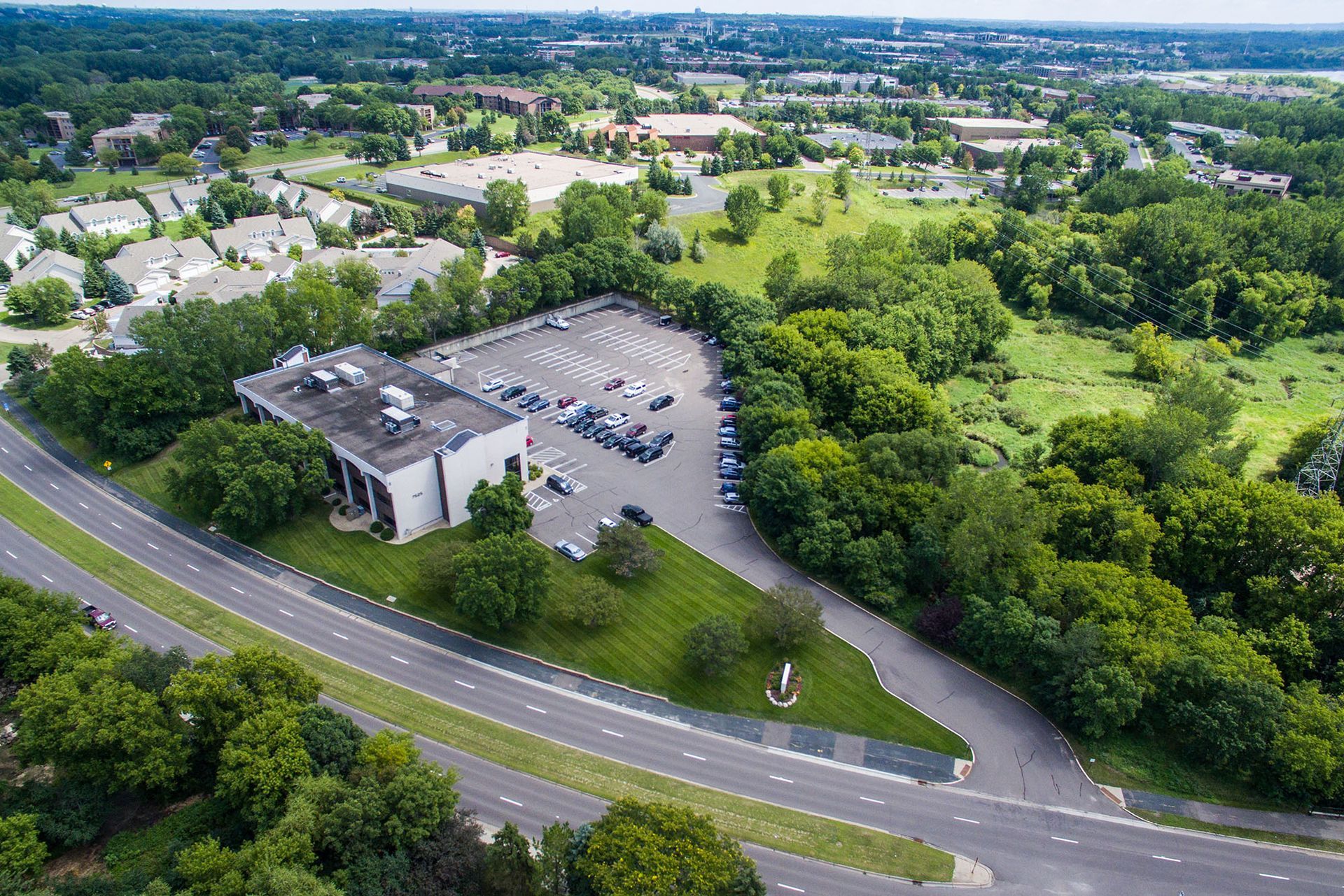 Aerial view of a building with a parking lot surrounded by trees, near a curved road.