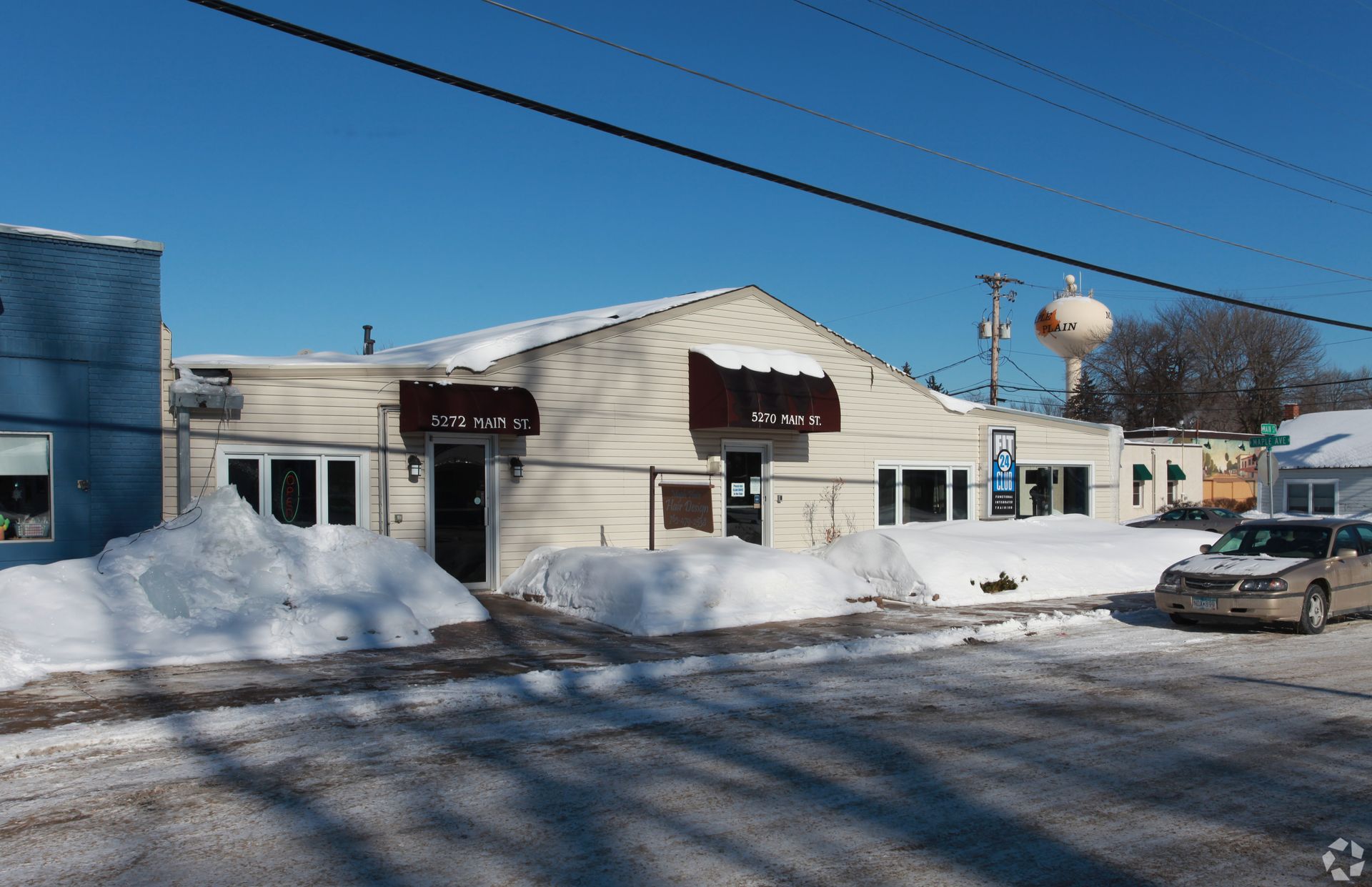 Exterior view of a snow-covered commercial building under a clear sky; a parked car is in view.