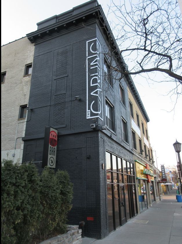 Dark gray building.  Street scene, brick facade, shrubs, and other shops.