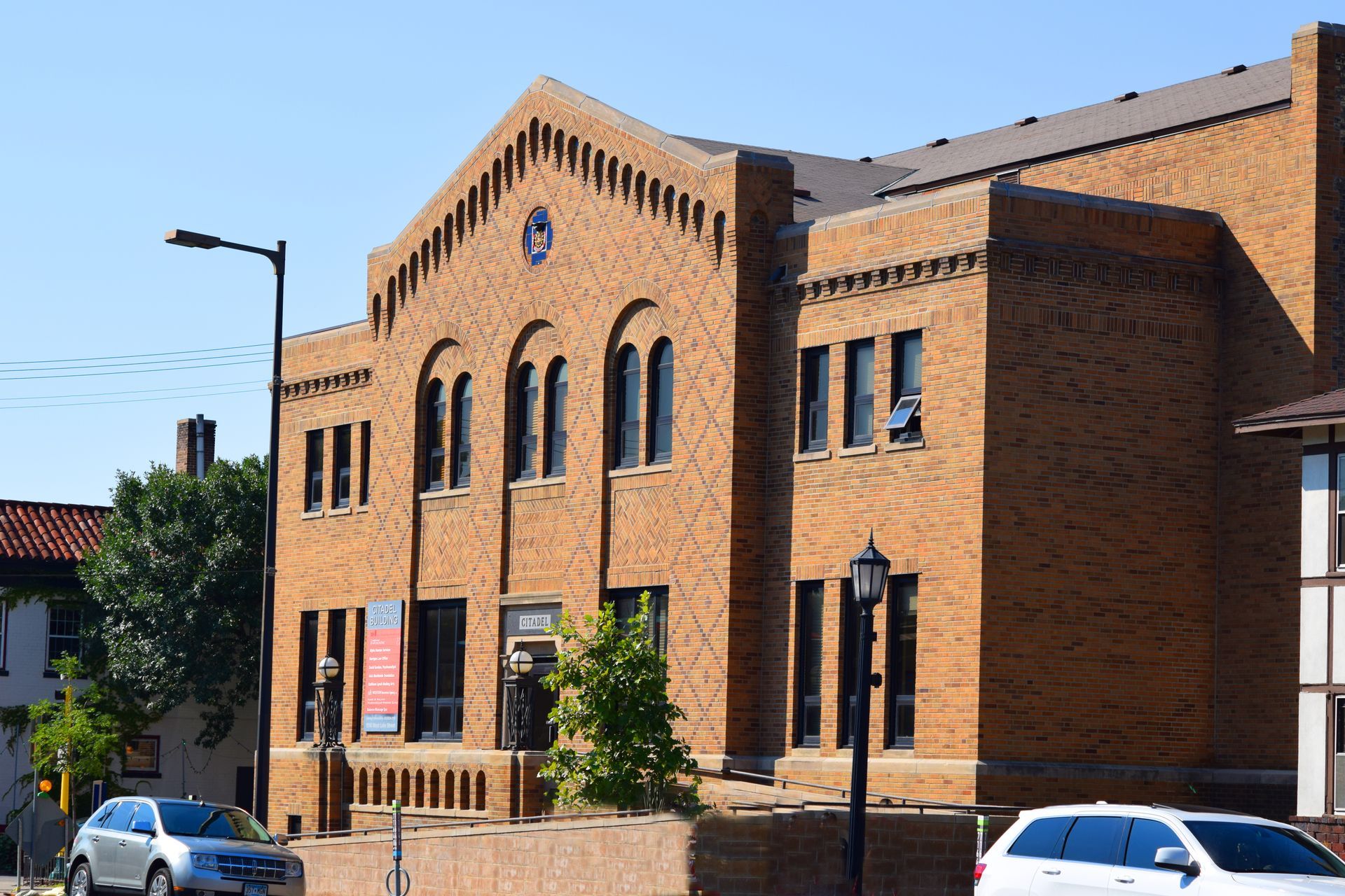 Brick building with arched windows, streetlights, and cars on a sunny day.