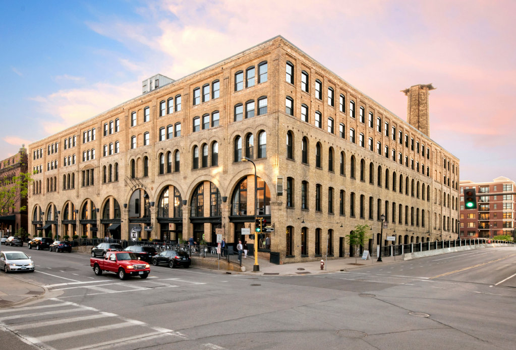 Large brick building on city street corner, vehicles and crosswalk visible.