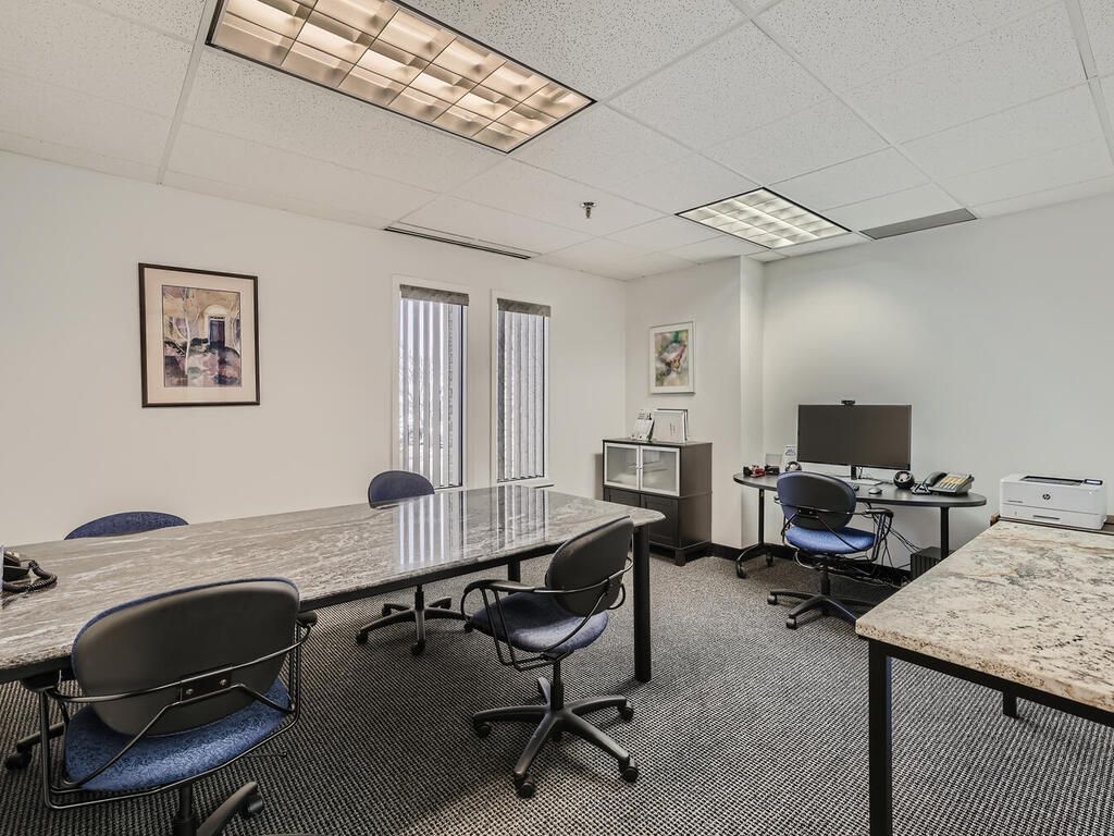 Office space with desks, chairs, computer monitors, windows, and fluorescent lighting.