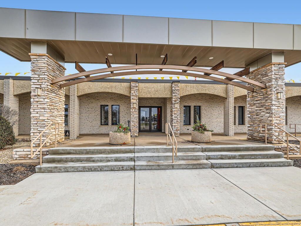Entrance to a building with brick columns and a curved canopy. Stone steps lead to the double doors.