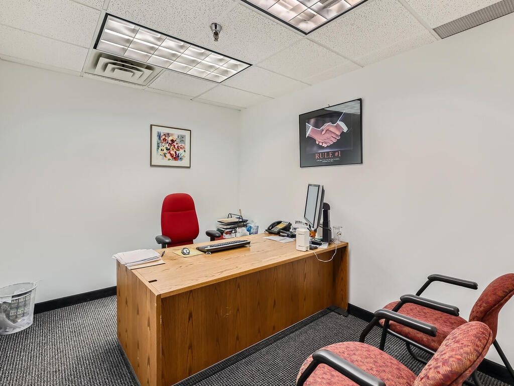 Small office with a desk, red chair, computer, phone, and two visitor chairs.