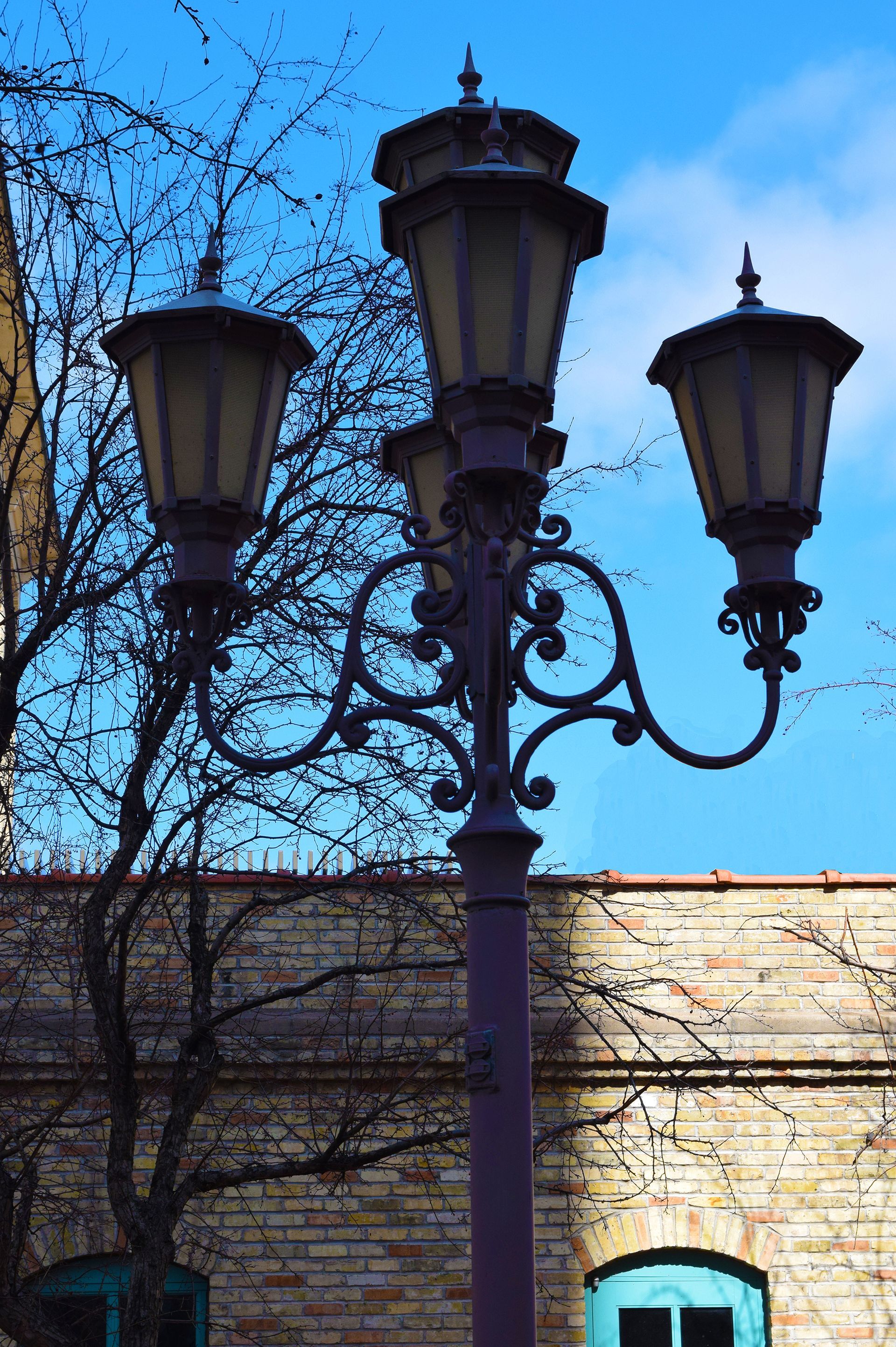 Ornate street lamp with three lanterns against a blue sky and brick building.