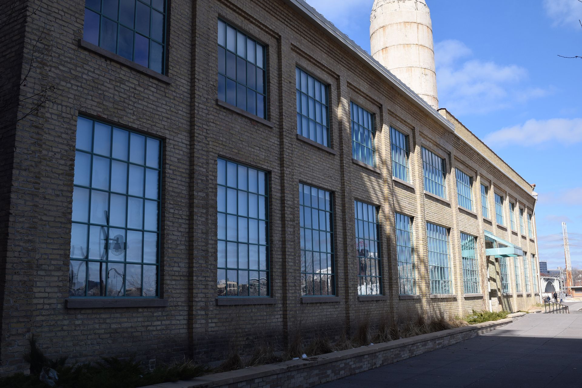 Brick industrial building with large windows, blue sky visible in the reflection.