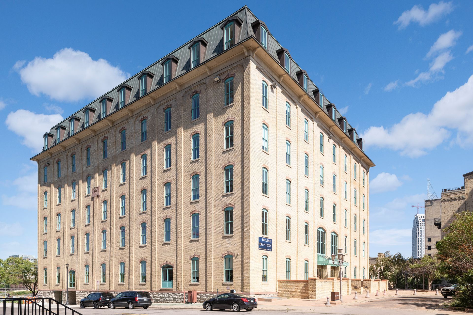 Brick building with many windows under a blue sky. Cars parked out front.