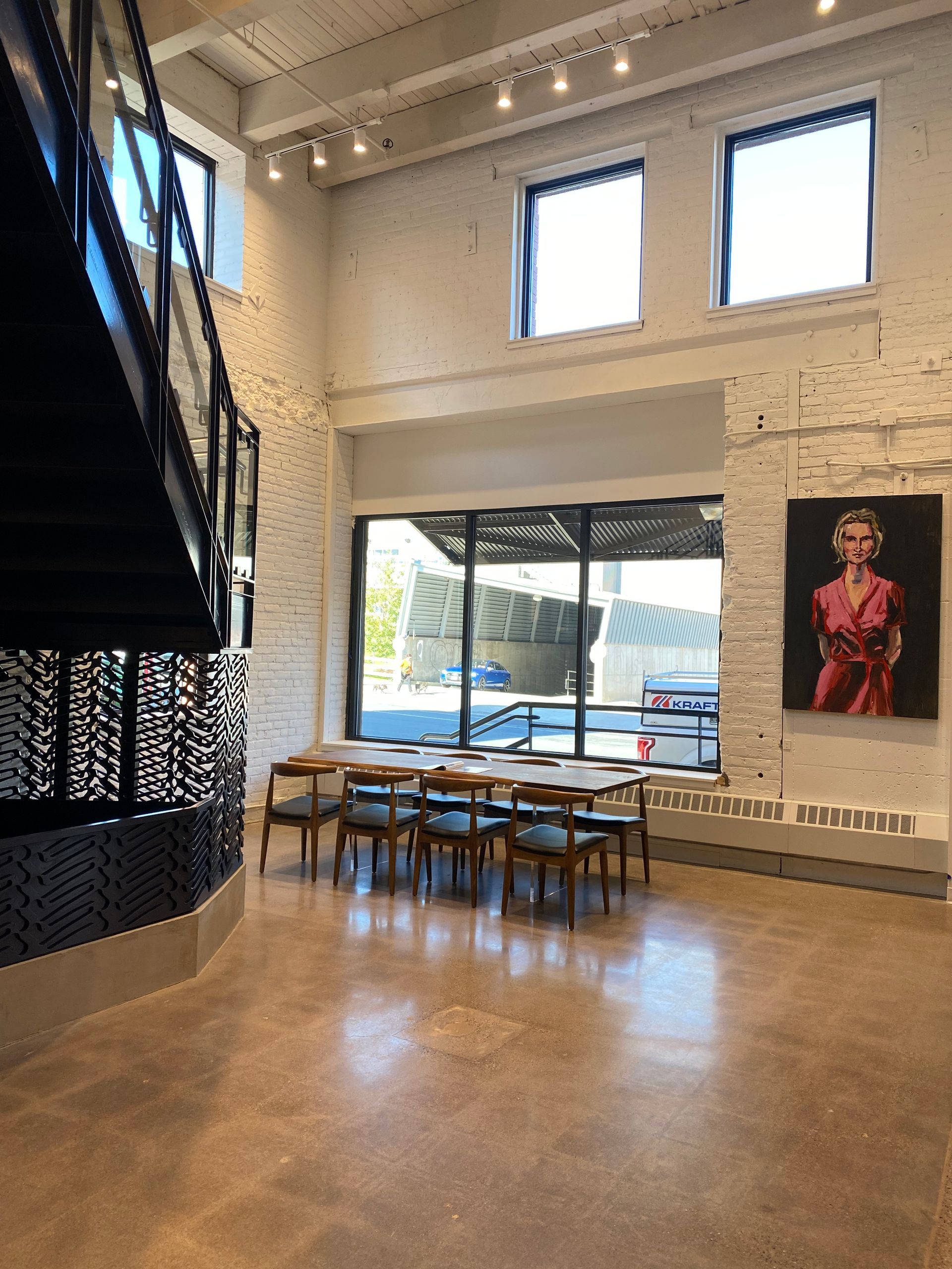 Spacious interior with a staircase, tables, chairs, and a painting; natural light streams through windows.