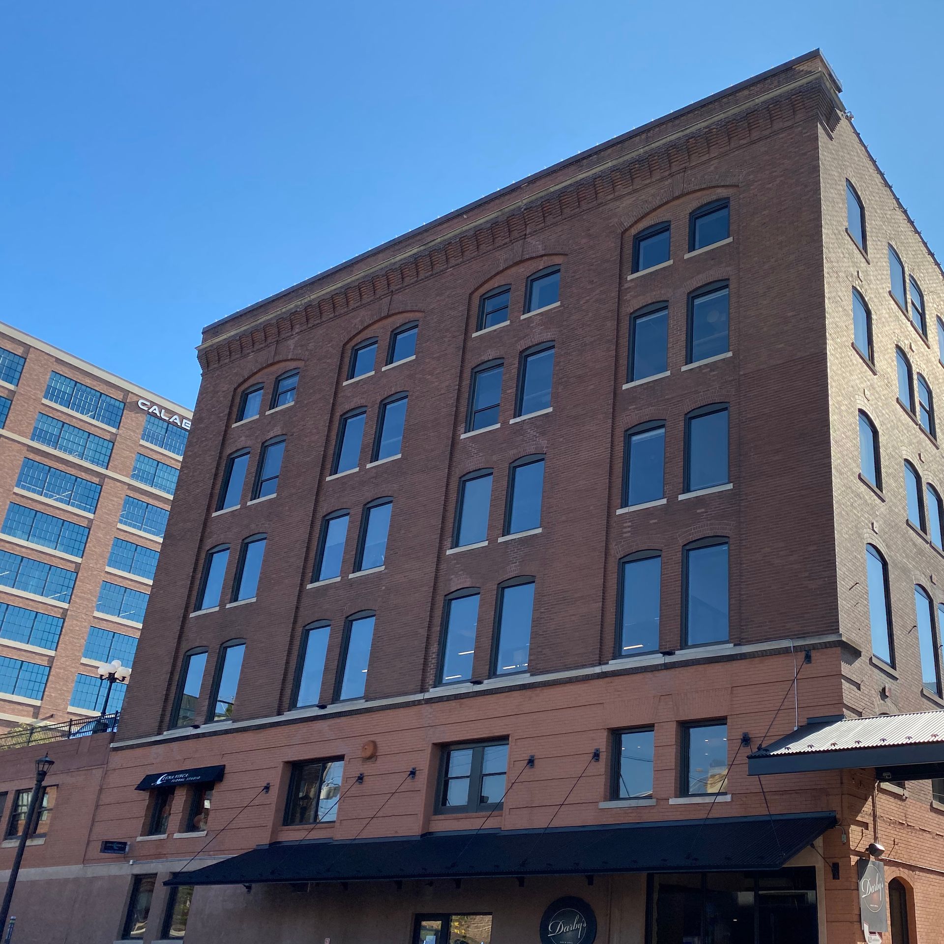 Brick building with many windows, a black awning, and a blue sky.
