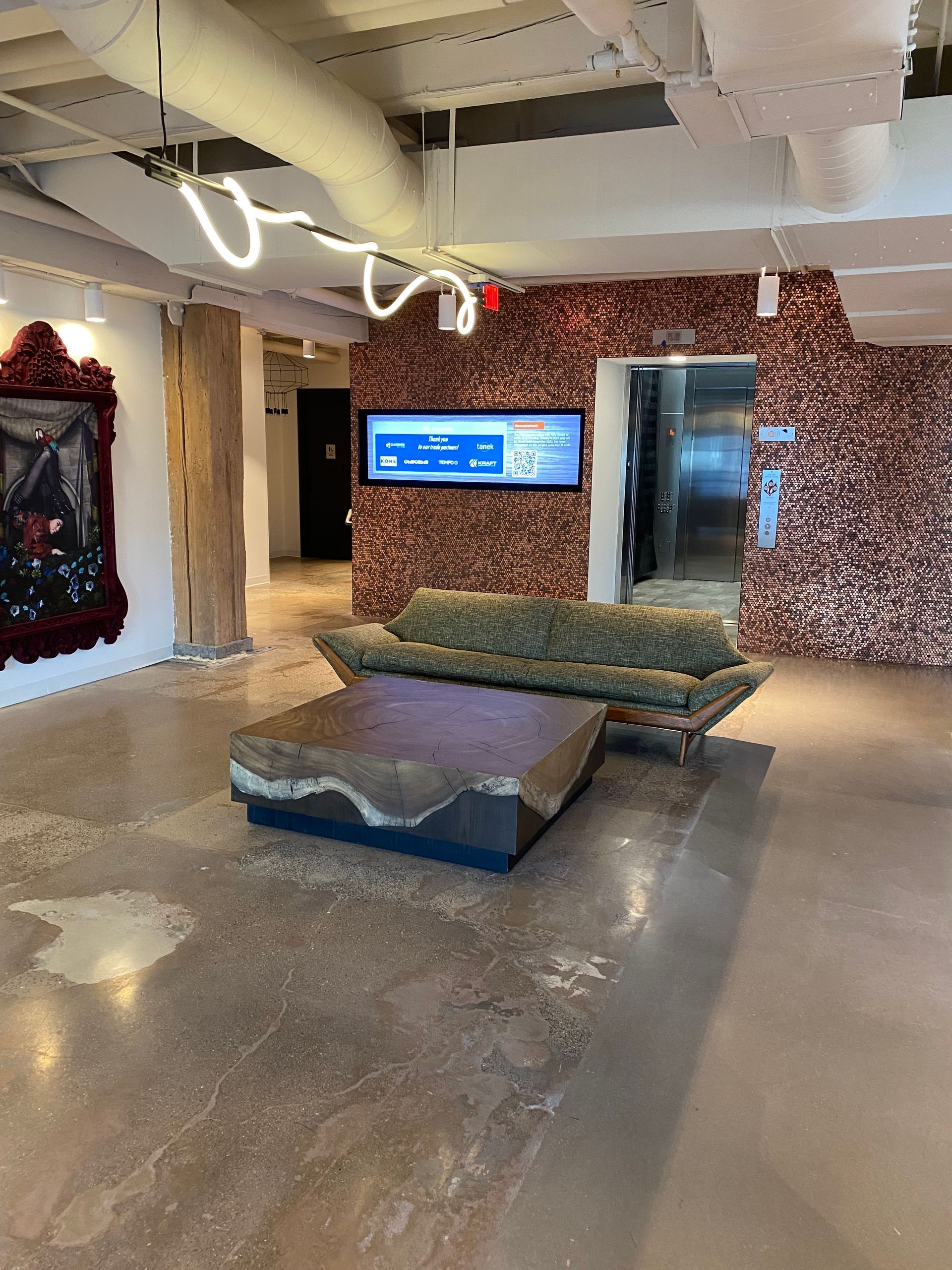 Lobby with modern furniture, stone coffee table, textured sofa, and a digital display on a copper penny-tiled wall.