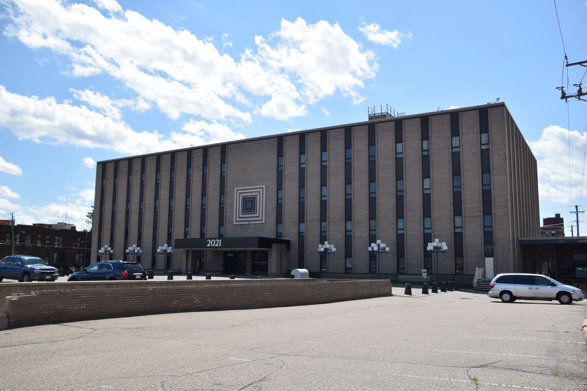 A large, light brick building with vertical lines and many windows, under a blue sky.