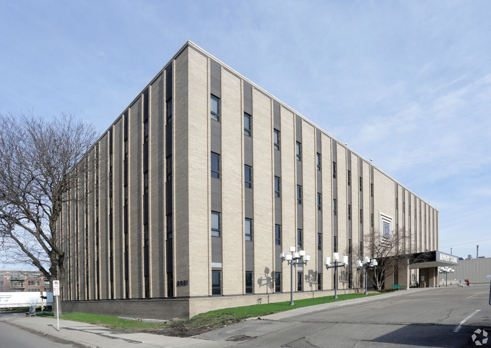 Four-story tan and gray building with vertical lines, windows, and trees on a corner lot.