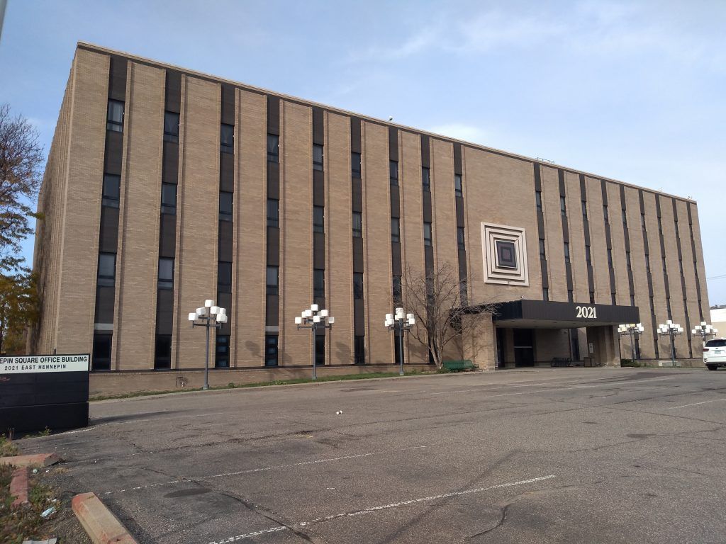 Brick building with dark vertical panels, small windows, and a concrete entrance.