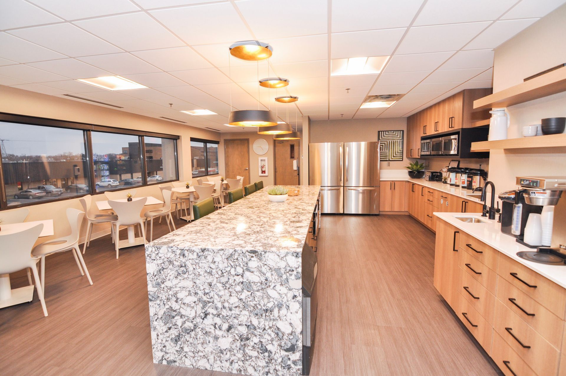 Spacious office kitchen with a large marble island, light wood cabinets, and seating area by the windows.