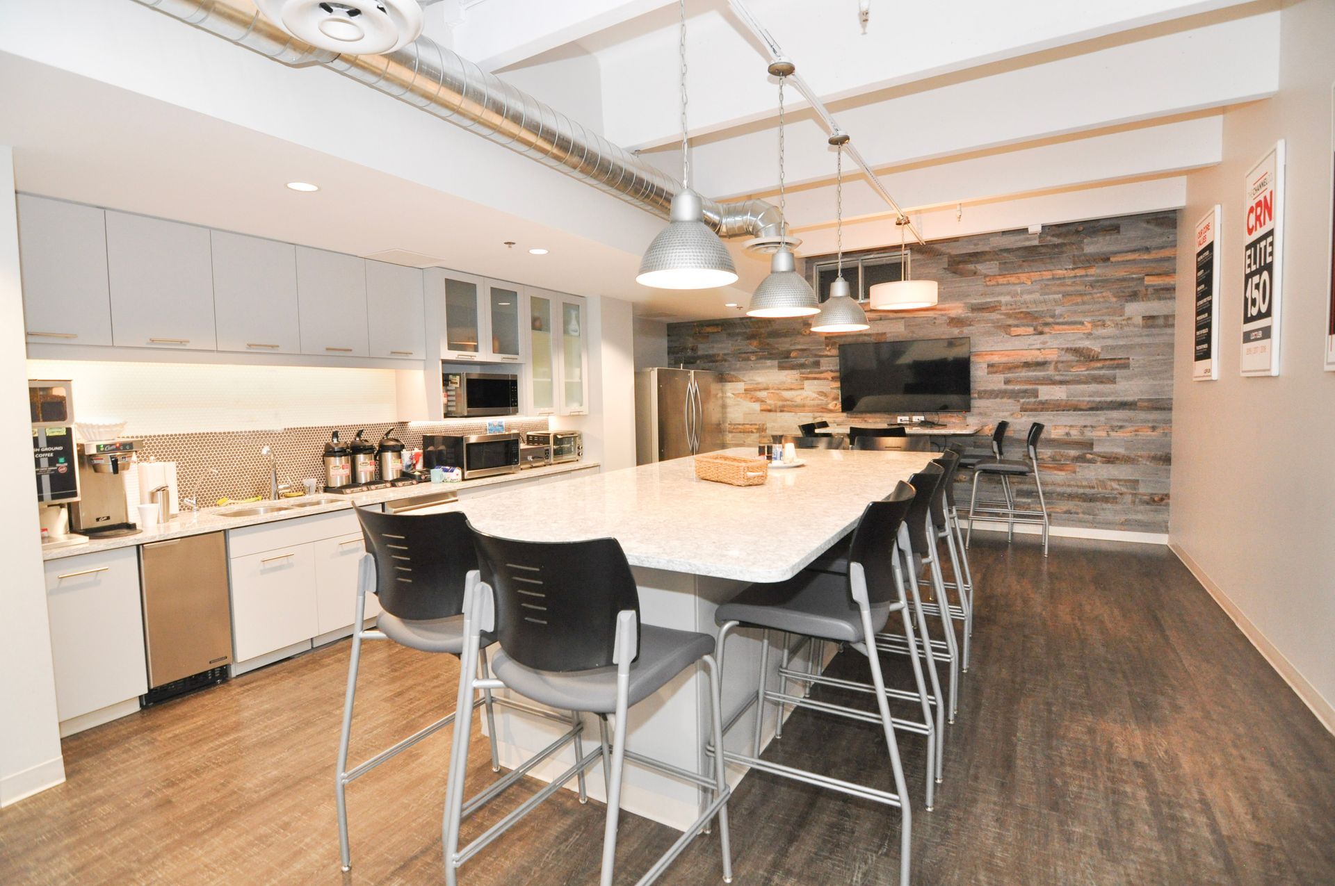 Modern office kitchen with white cabinets, a large island, and a stone accent wall.