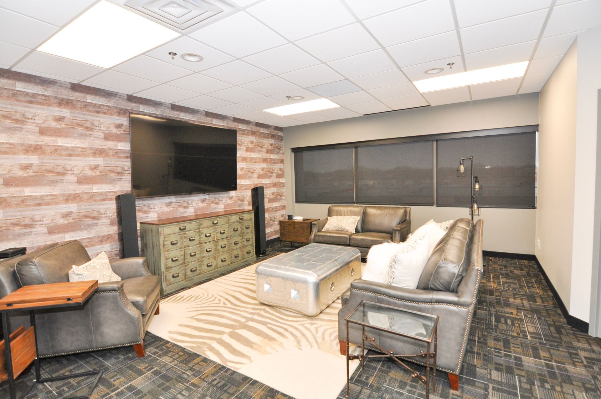 Relaxation room with gray leather couches, TV, and brick accent wall.
