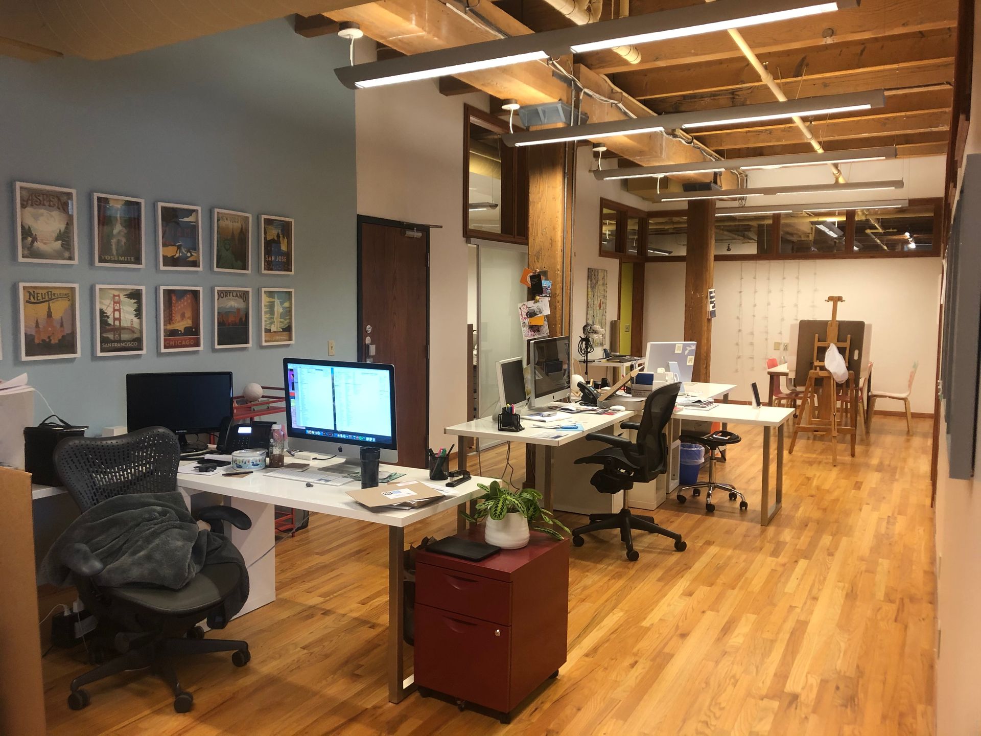 Office interior with desks, computers, artwork, wood floors and ceiling beams.