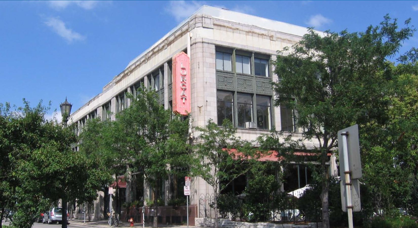 Exterior view of a two-story building with a red sign; trees line the sidewalk.