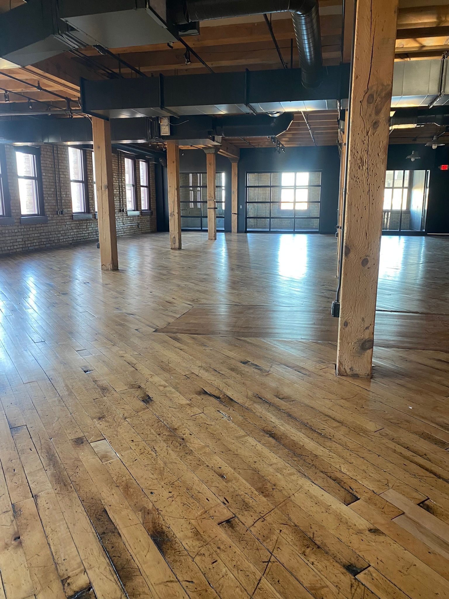 Empty wood-floored office space with exposed beams and columns. Doors and windows let in natural light.