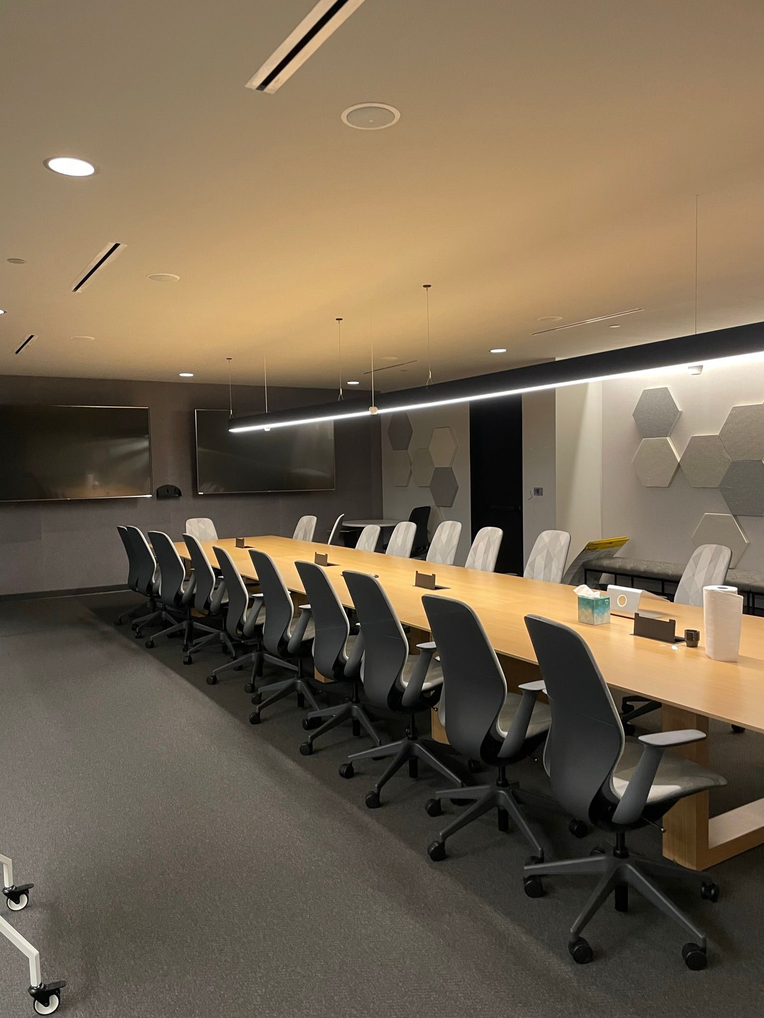 Conference room with a long wooden table, chairs, and a large screen.