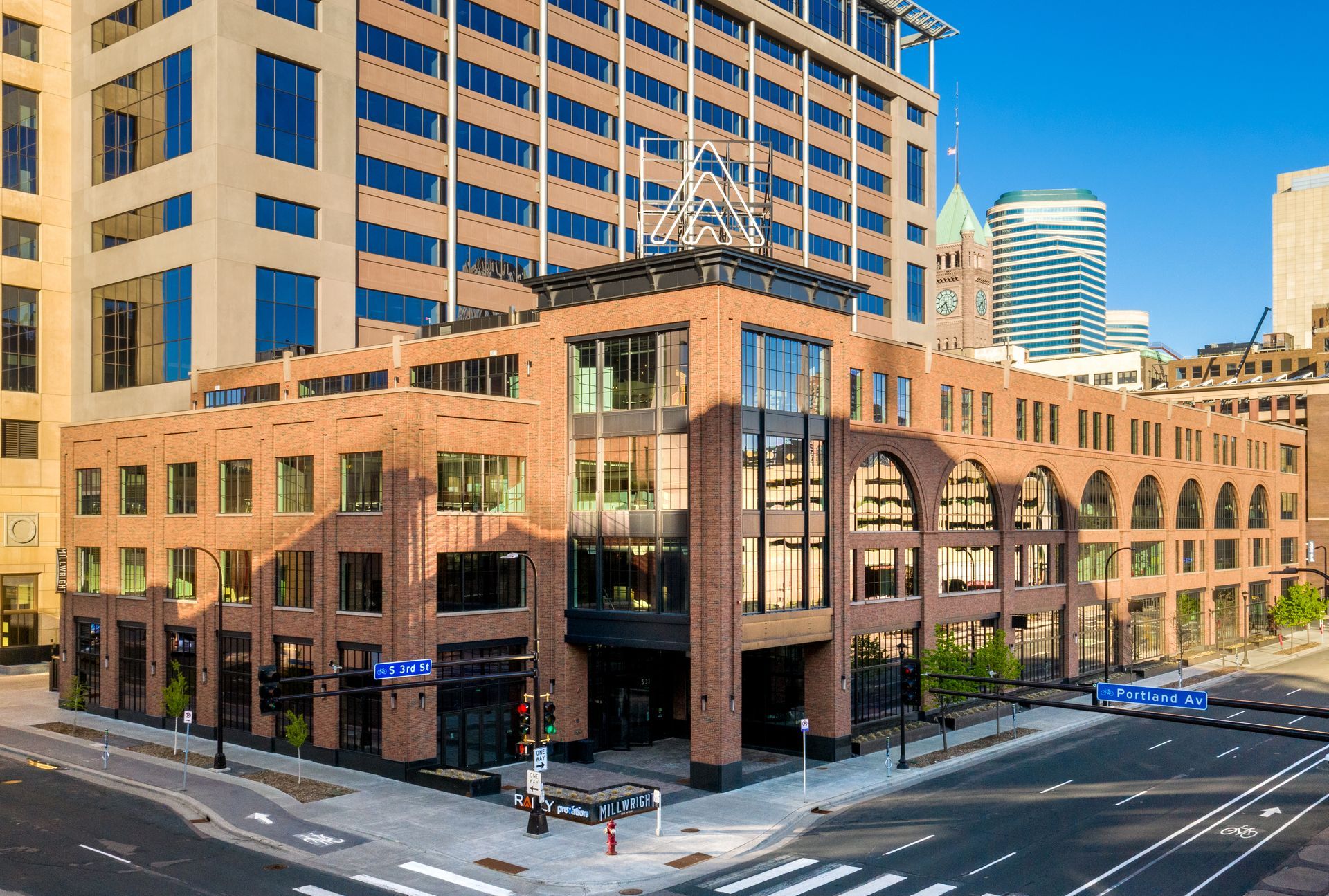Brick building with arched windows in a city setting. Tall glass and steel building behind it.