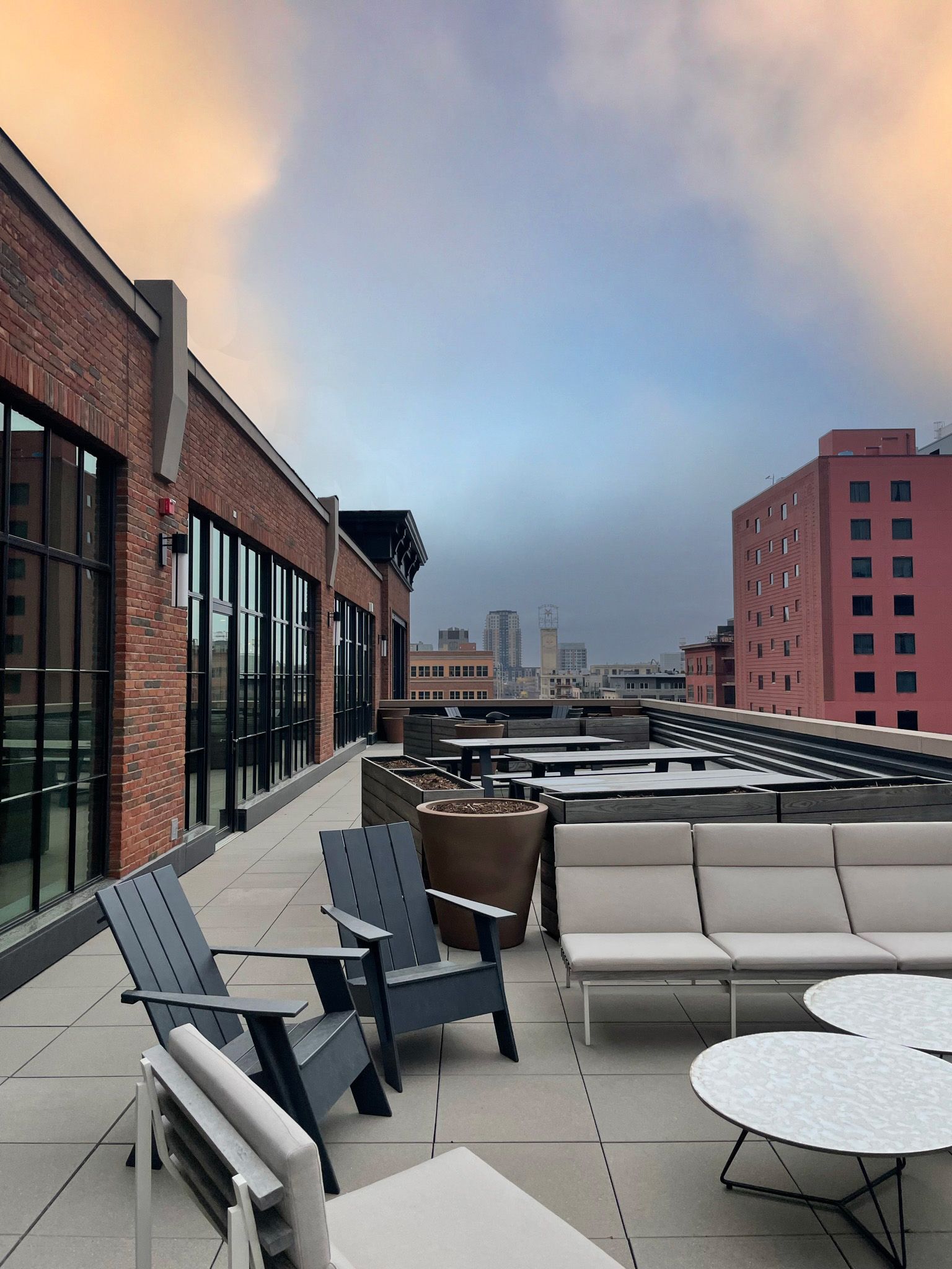 Rooftop patio with seating, brick building, city skyline background, overcast sky.