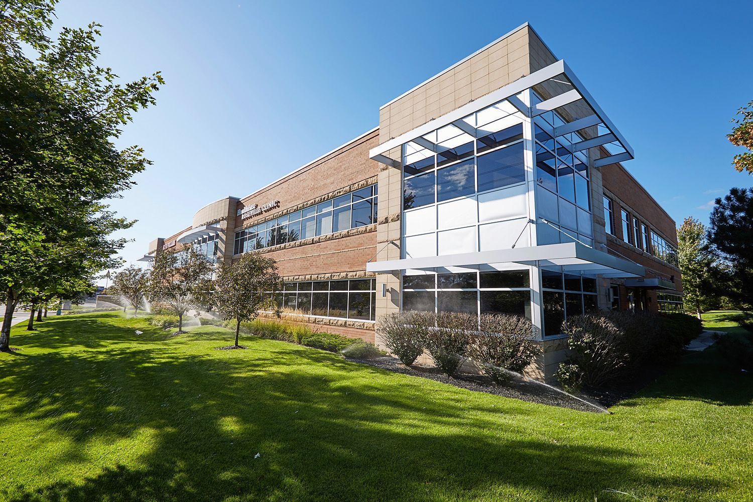 Two-story brick and glass office building with landscaping, under a blue sky.