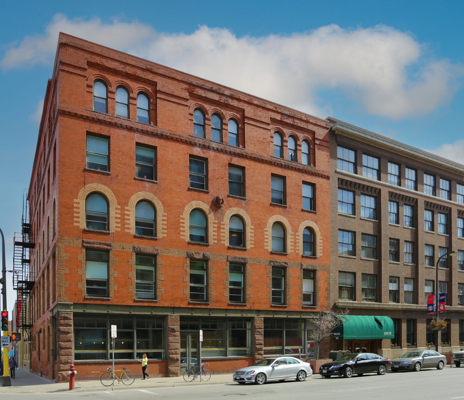 Red brick building with arched windows, parked cars on street, blue sky.