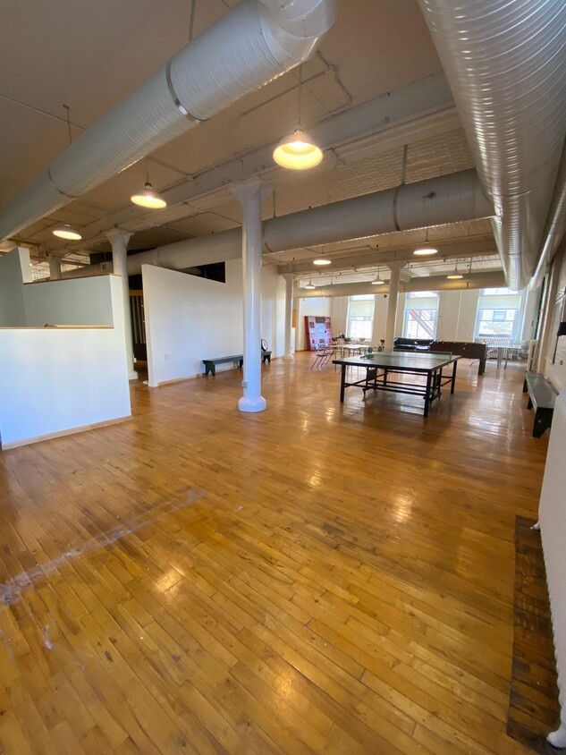 Spacious room with hardwood floors, white walls, exposed ductwork, and round columns; a ping pong table is centered.
