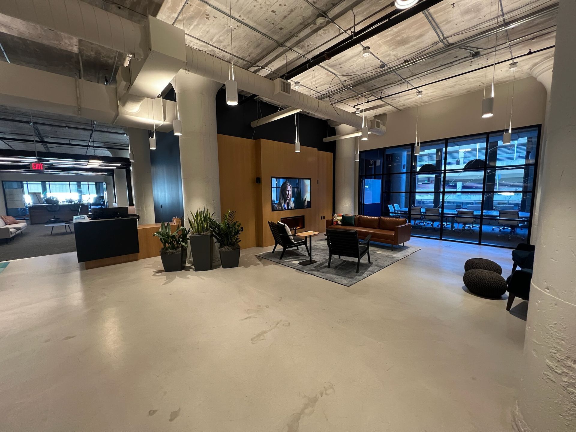 Spacious modern office lobby with seating areas, large windows, concrete floors, and potted plants.