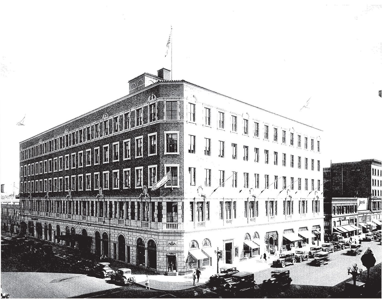 Large historic office & retail building on a city street with shops on the ground floor; cars parked nearby.