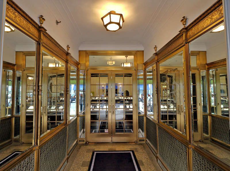 Hallway with gold-framed mirrors and doors reflecting the interior. A dark rug lies in the center.