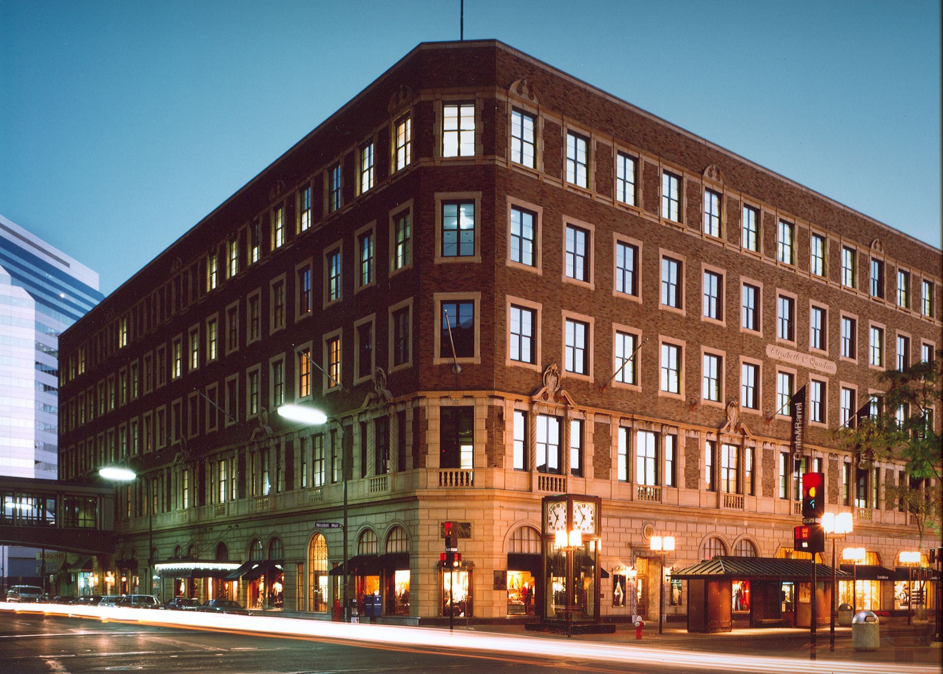 Brick building at night with lighted windows and storefronts on a city street.